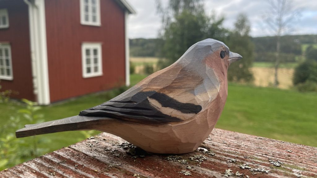 Fågel i trä som sitter på en bräda och tittar ut över landskapet