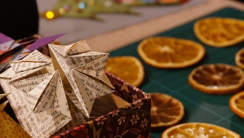 Stjärna i papper, torkade apelsinskivor och en glittrig julgran i papper i bakgrunden.